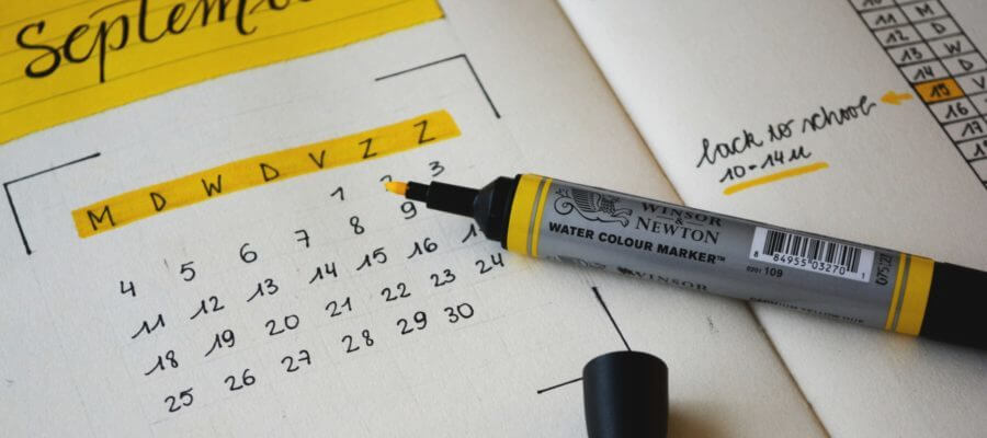 A yellow highlighter rests on the page of a planner - the days of the week of a September monthly calendar are highlighted.